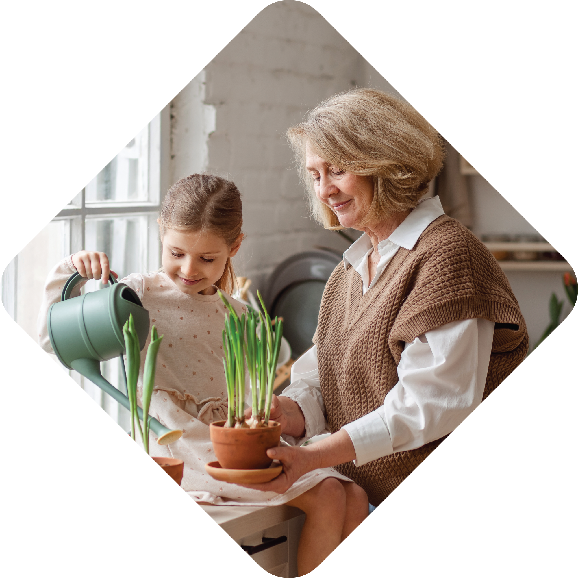 An photo of two people. On the left is a young girl holding a watering pitcher. On the right is an older woman holding a plant