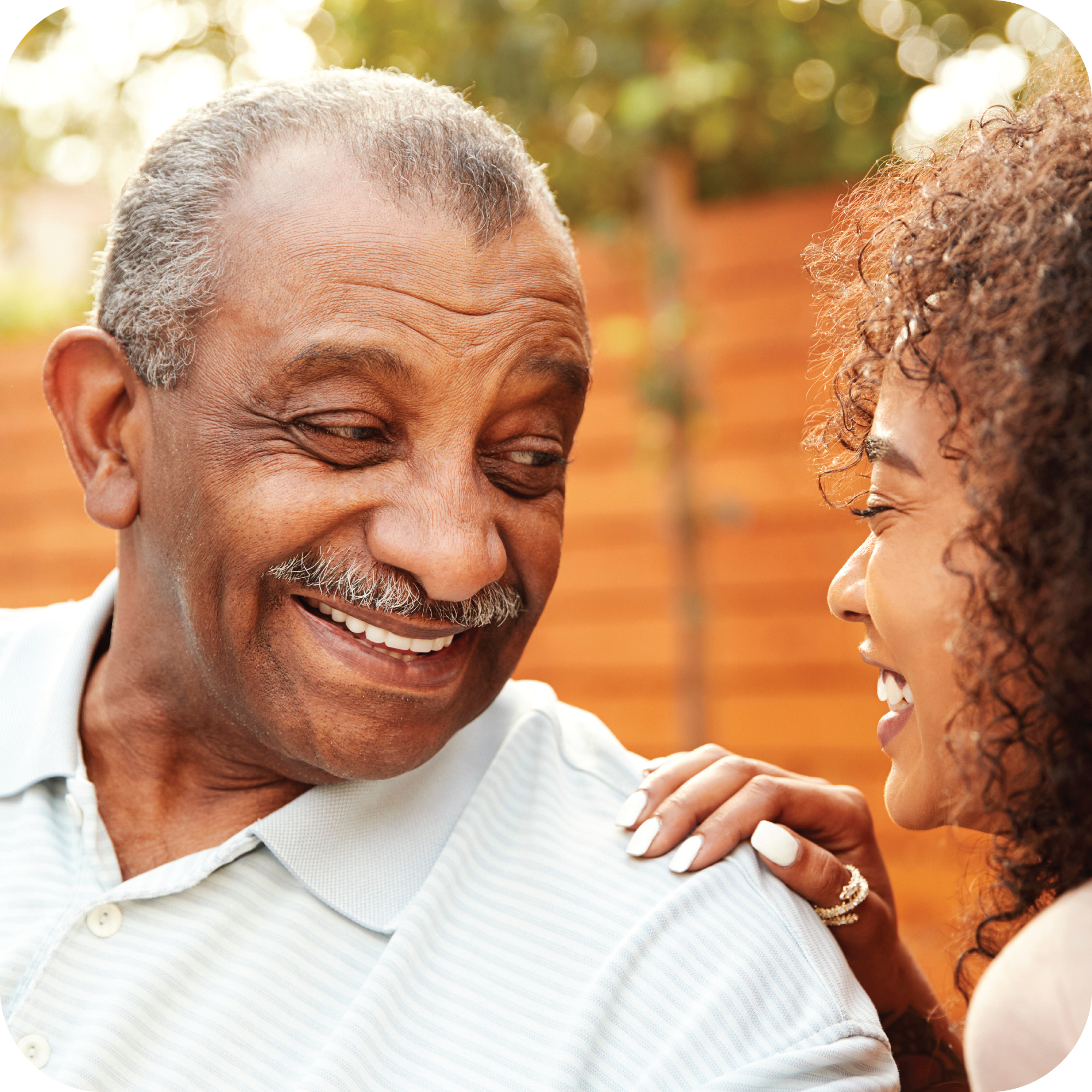 An photo of two people. On the left is an older man who is similing. On the right is an older woman looking at the man